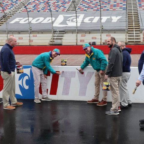 Steven C. Smith, president and chief executive officer of Food City (middle left), along with Bristol Motor Speedway president Jerry Caldwell (middle right), and Kevin Stafford, vp of marketing for Food City (left of Smith) are surrounded by Food City store managers as they apply some of the final brush strokes of the throwback paint job to the track walls for the upcoming Food City 500, March 17.